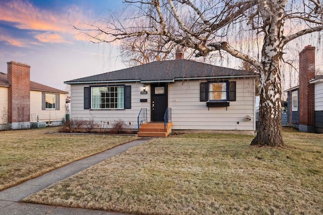 bungalow featuring a chimney, a lawn, and roof with shingles