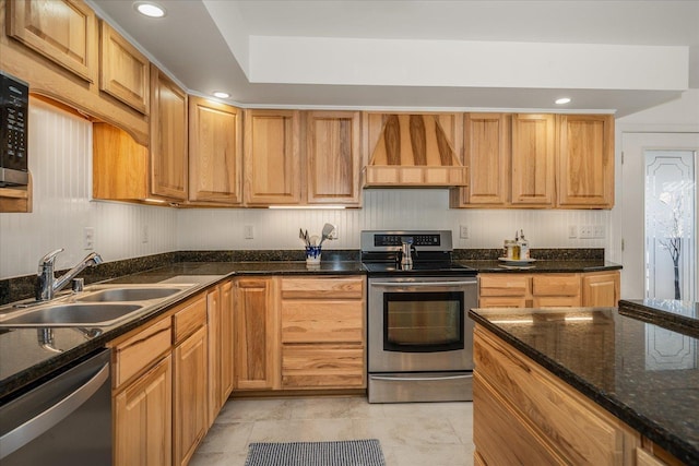 kitchen with dark stone counters, stainless steel appliances, premium range hood, a sink, and recessed lighting