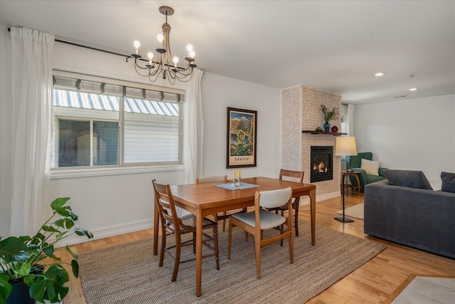 dining area with light wood-style flooring, a fireplace, baseboards, and a notable chandelier