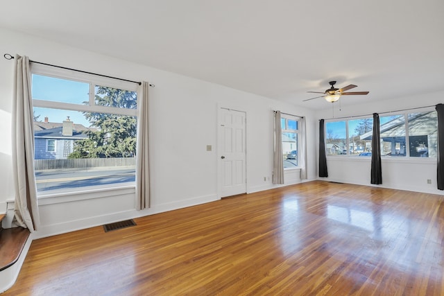 empty room with a ceiling fan, visible vents, baseboards, and wood finished floors