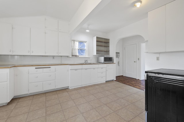 kitchen with arched walkways, light countertops, black range with electric stovetop, white cabinetry, and vaulted ceiling