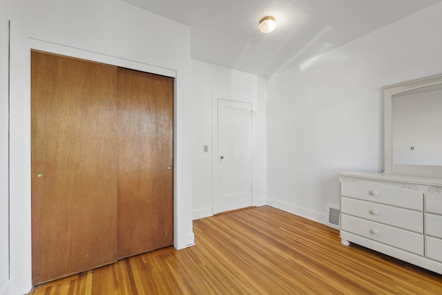 unfurnished bedroom featuring a closet, wood finished floors, visible vents, and baseboards