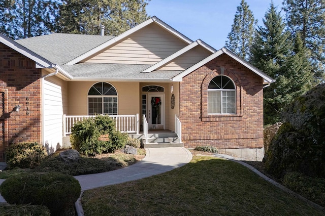 ranch-style house with a porch, a front yard, brick siding, and roof with shingles