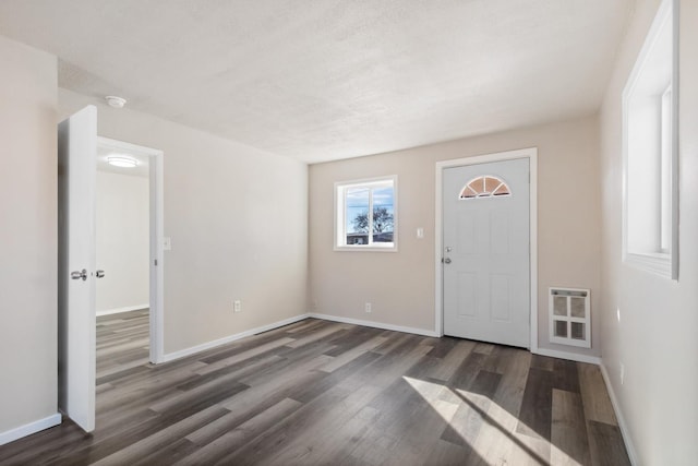 foyer entrance featuring baseboards, a textured ceiling, wood finished floors, and heating unit