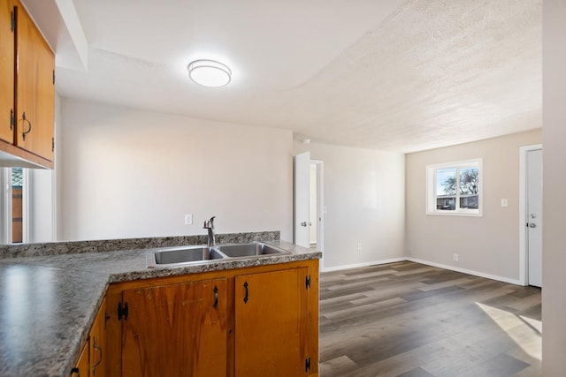 kitchen with dark wood-type flooring, brown cabinetry, a sink, and baseboards