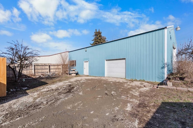 view of outdoor structure with a garage, an outbuilding, fence, and dirt driveway