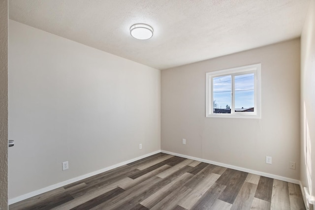 spare room with a textured ceiling, wood finished floors, and baseboards