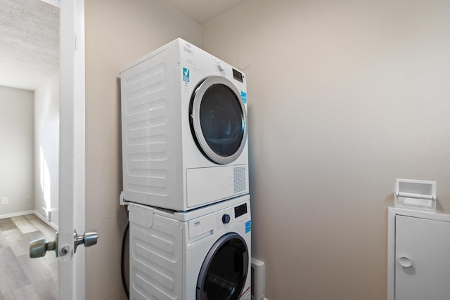 laundry area featuring wood finished floors, stacked washer and clothes dryer, and laundry area