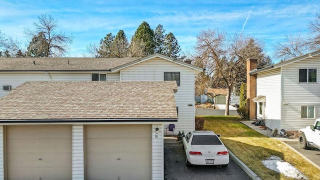 view of front of house featuring a garage, a front yard, and roof with shingles