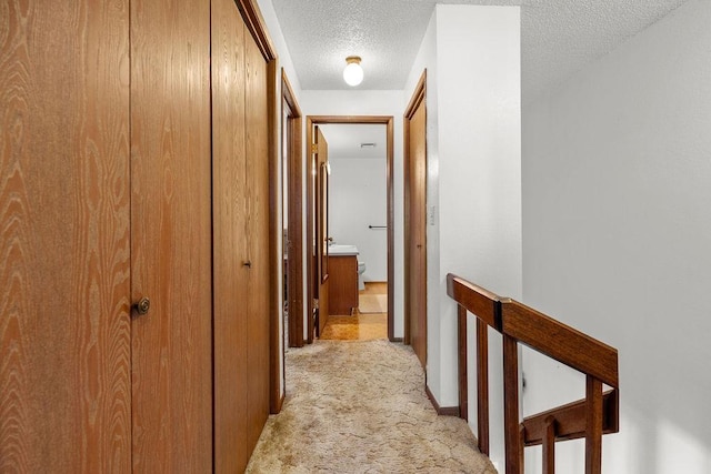 corridor featuring an upstairs landing, a textured ceiling, and light colored carpet