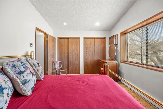 bedroom featuring multiple closets, vaulted ceiling, a textured ceiling, and baseboard heating