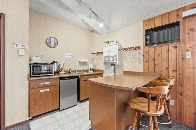 kitchen with brown cabinetry, a breakfast bar, a peninsula, a textured ceiling, and stainless steel dishwasher