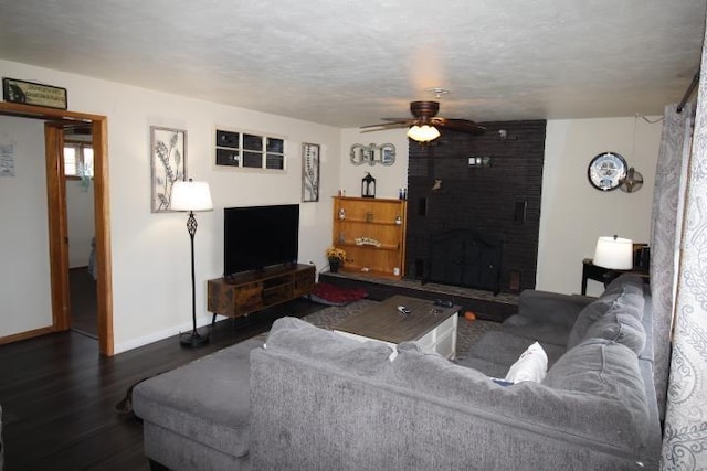 living area with dark wood-style floors, a fireplace, ceiling fan, a textured ceiling, and baseboards