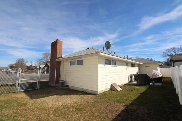 rear view of house featuring a lawn, a chimney, fence, and a gate