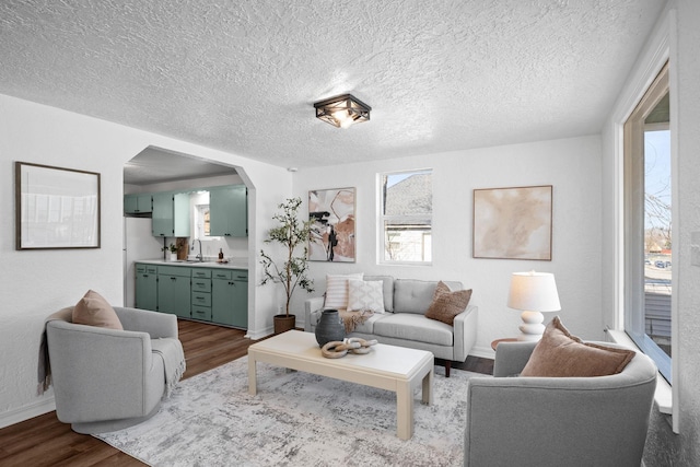 living area with arched walkways, dark wood-type flooring, a textured ceiling, and baseboards