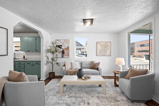 living room featuring a textured ceiling, arched walkways, wood finished floors, and baseboards