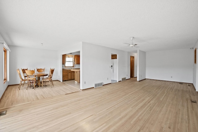living area featuring a textured ceiling, light wood-style flooring, and visible vents