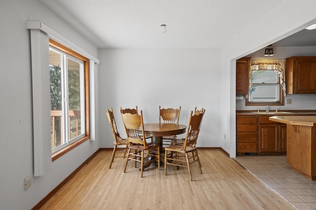 dining space with a textured ceiling, light wood-type flooring, and baseboards