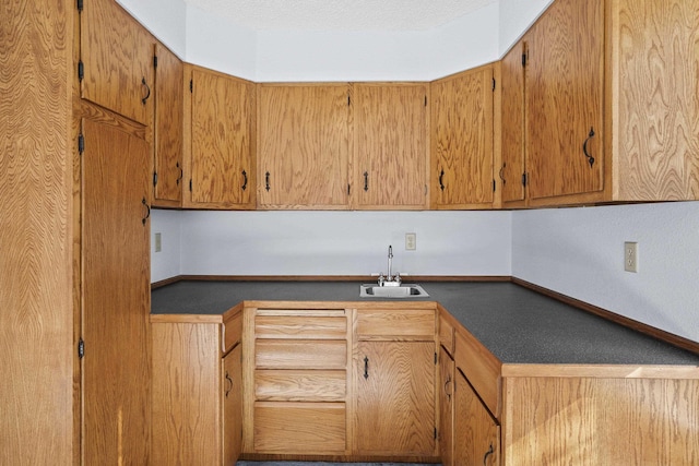 kitchen featuring dark countertops, a sink, and baseboards