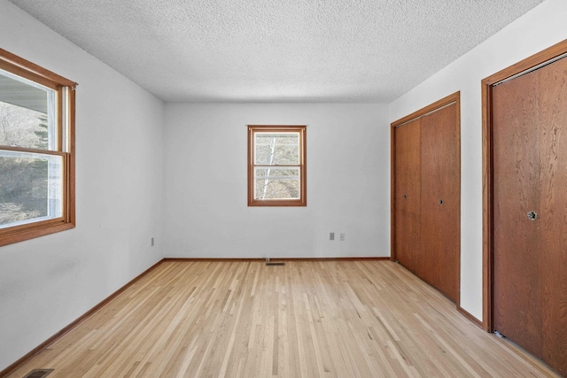unfurnished bedroom with a textured ceiling, light wood-style flooring, visible vents, baseboards, and multiple closets