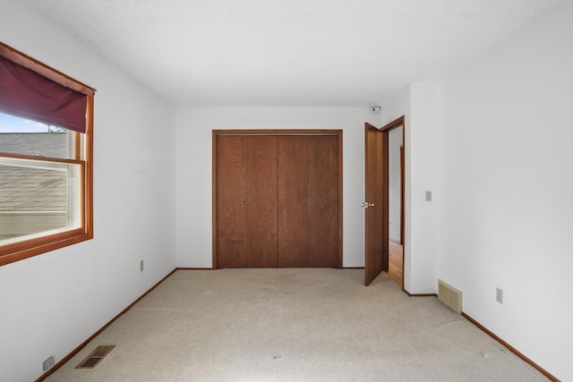 unfurnished bedroom featuring baseboards, a closet, visible vents, and light colored carpet