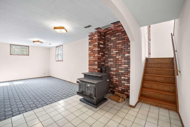 basement with visible vents, a wood stove, light carpet, baseboards, and stairs