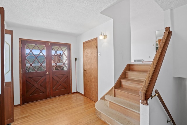 foyer entrance with stairway, light wood-style flooring, visible vents, and a textured ceiling