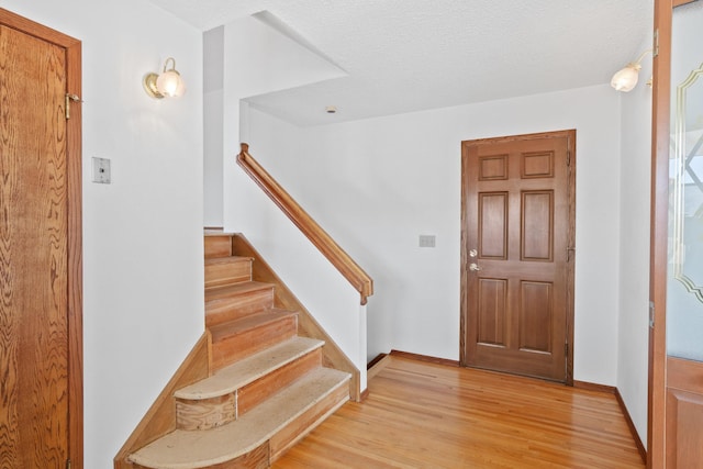 entrance foyer with stairs, light wood finished floors, a textured ceiling, and baseboards