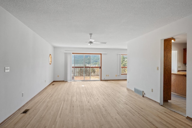 unfurnished living room with ceiling fan, light wood finished floors, a textured ceiling, and visible vents