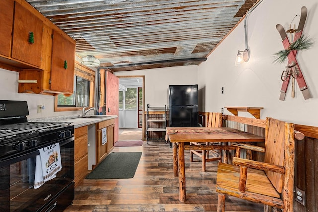 kitchen with a sink, light countertops, brown cabinets, dark wood-style floors, and black appliances