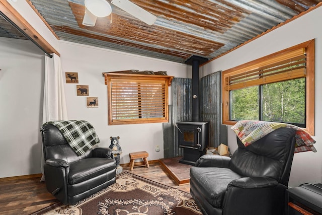 sitting room with a ceiling fan, a wood stove, baseboards, and wood finished floors