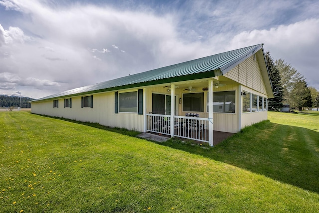 view of side of property featuring covered porch, a ceiling fan, metal roof, and a lawn