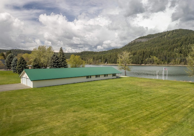 view of yard featuring a forest view, a detached garage, an outbuilding, a water view, and a pole building