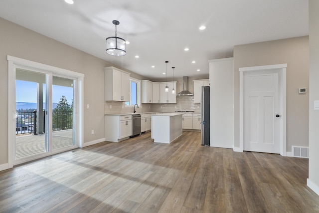 kitchen featuring appliances with stainless steel finishes, a center island, light countertops, wall chimney range hood, and backsplash