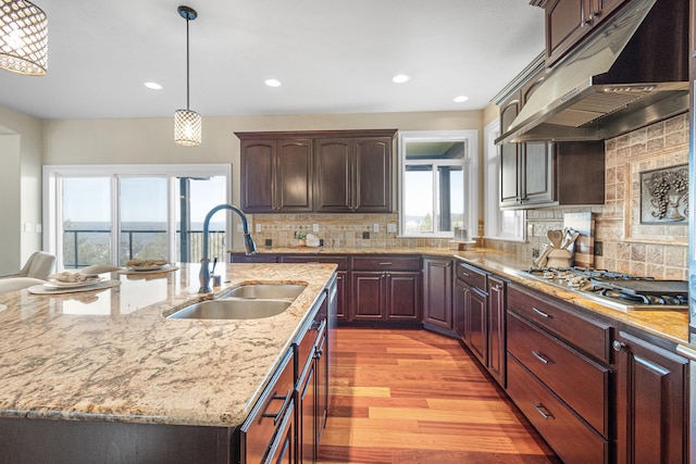 kitchen featuring under cabinet range hood, a sink, light wood-style floors, decorative backsplash, and stainless steel gas stovetop