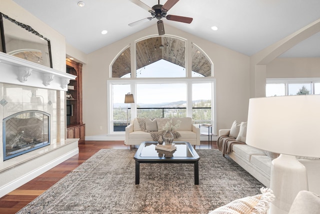 living area with high vaulted ceiling, a tile fireplace, recessed lighting, wood finished floors, and baseboards