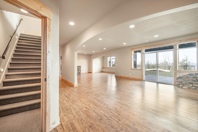 unfurnished living room featuring arched walkways, recessed lighting, baseboards, and light wood-style floors