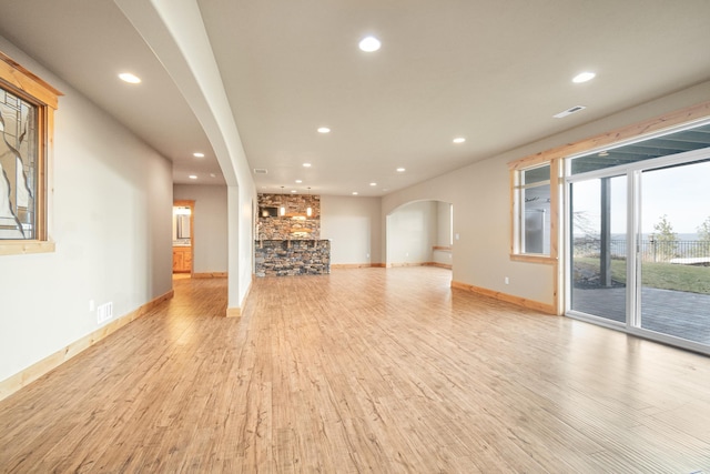 unfurnished living room with visible vents, arched walkways, baseboards, recessed lighting, and light wood-style flooring