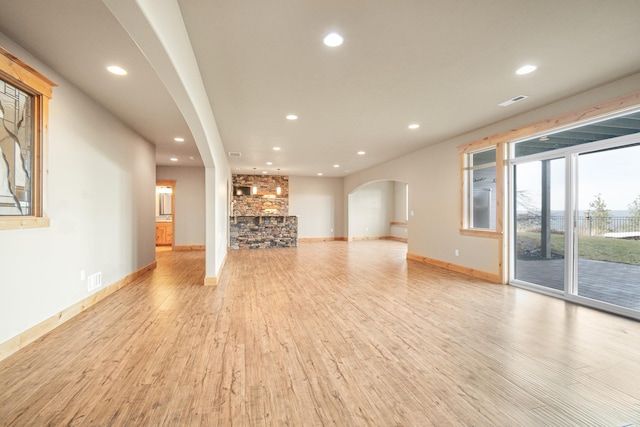 unfurnished living room with arched walkways, recessed lighting, baseboards, and light wood-style floors