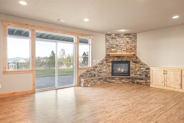 unfurnished living room featuring a healthy amount of sunlight, visible vents, wood finished floors, and a stone fireplace