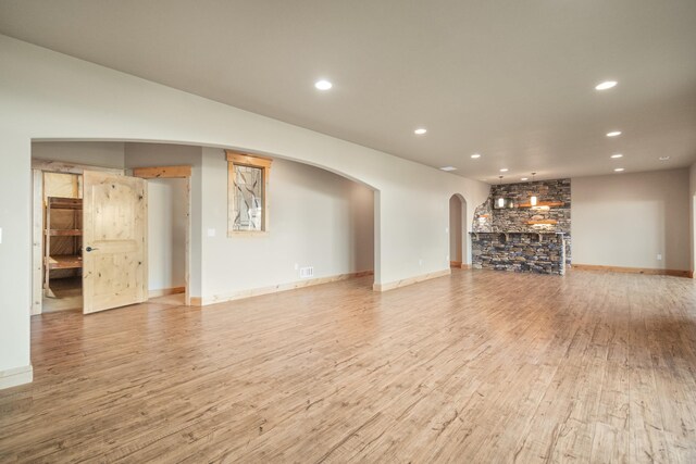 unfurnished living room featuring light wood finished floors, baseboards, visible vents, arched walkways, and recessed lighting