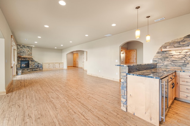 kitchen featuring arched walkways, recessed lighting, visible vents, a stone fireplace, and light wood-type flooring