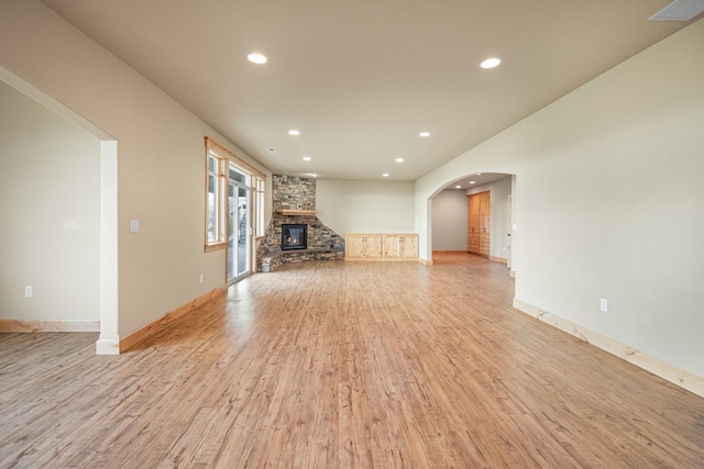 unfurnished living room with arched walkways, a stone fireplace, recessed lighting, visible vents, and light wood finished floors