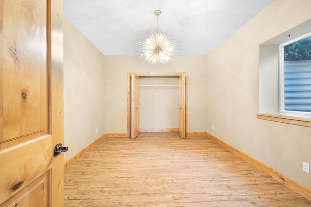 unfurnished room featuring a chandelier, light wood-style flooring, and baseboards