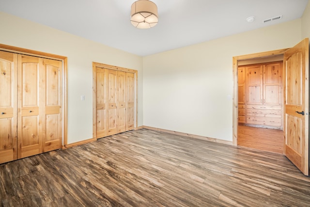 unfurnished bedroom featuring two closets, baseboards, visible vents, and wood finished floors