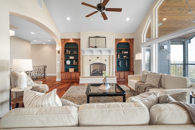 living area featuring arched walkways, visible vents, a tiled fireplace, wood finished floors, and baseboards