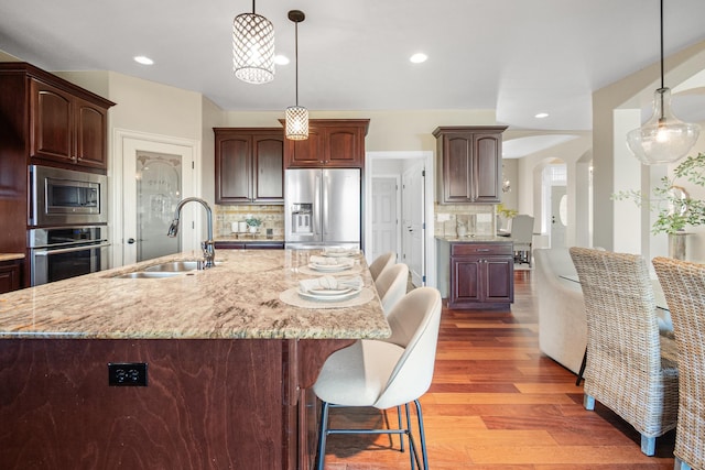 kitchen with arched walkways, appliances with stainless steel finishes, wood finished floors, light stone countertops, and a sink