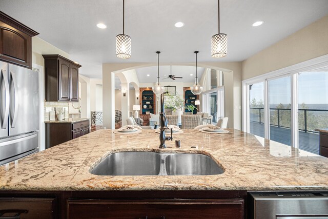 kitchen with arched walkways, freestanding refrigerator, open floor plan, dark brown cabinetry, and a sink