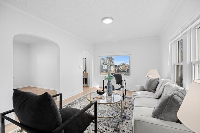 living room featuring arched walkways, a textured ceiling, light wood-style flooring, and baseboards