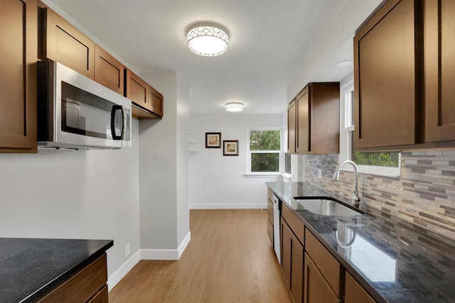 kitchen featuring a sink, baseboards, decorative backsplash, dark stone counters, and stainless steel microwave